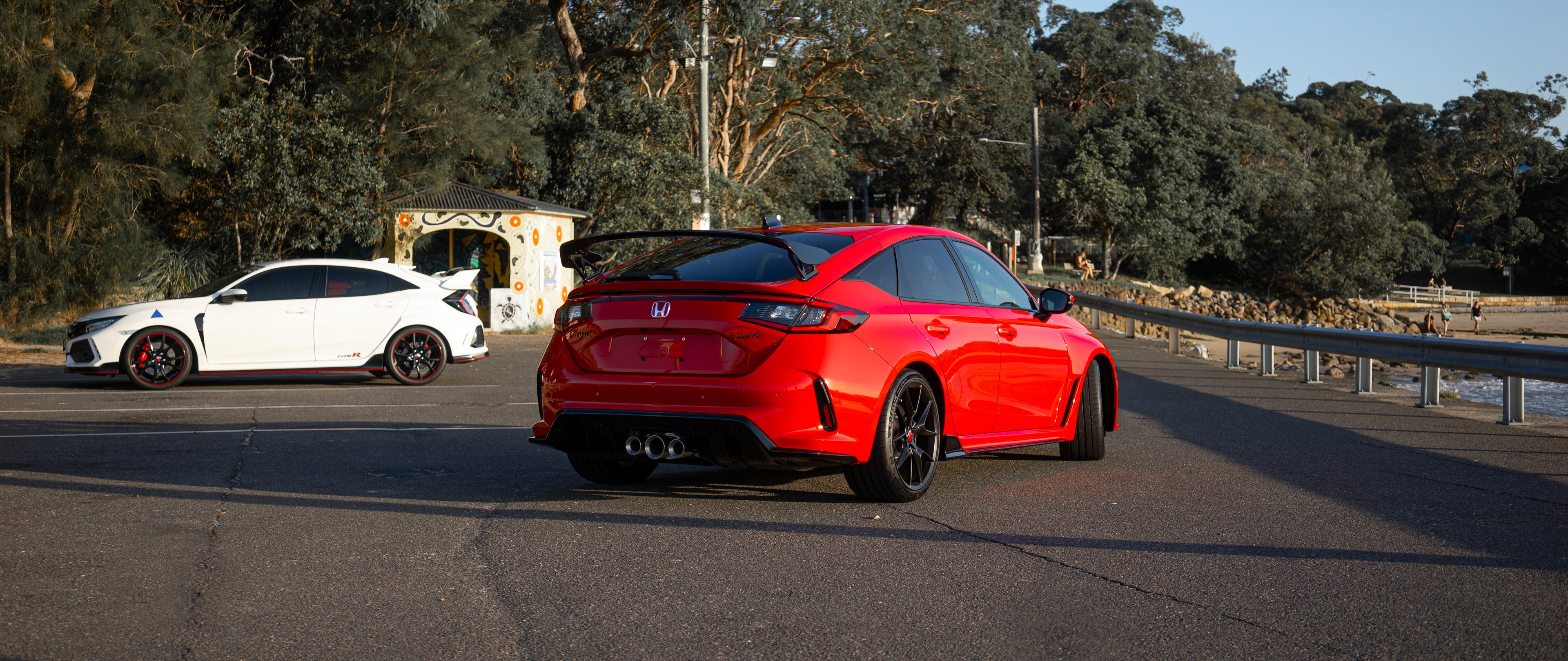 A warm afternoon sunset on an australian pier near a beach glowing on the rear view of a rallye red honda civic type r FL5 and a championship white honda civic type r FK8